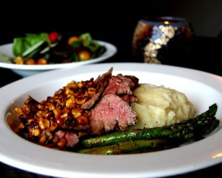 Back cast cafe steak dinner on white plate and side salad behind it on black background